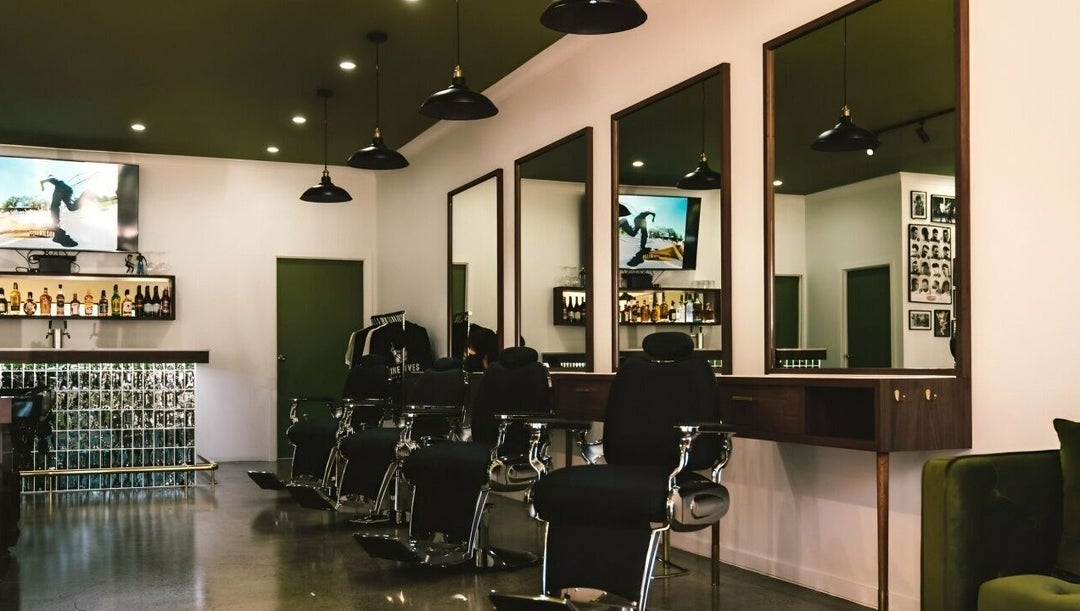 Nine Lives Barbershop interior — olive green ceiling, walnut wood stations, black barber chairs, polished concrete floors